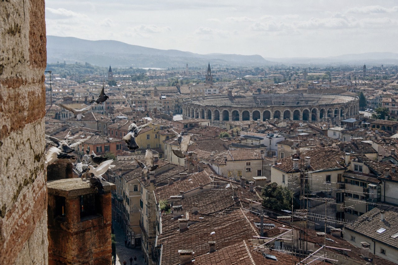 View of Verona's historic centre from above, showing the Arena amphitheatre and red-tiled rooftops, no text, no logos, no people
