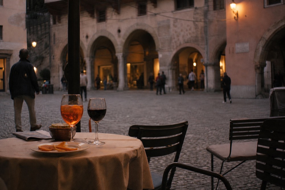 An evening aperitivo table with a spritz and wine glasses in a Verona square, no text, no logos, no people