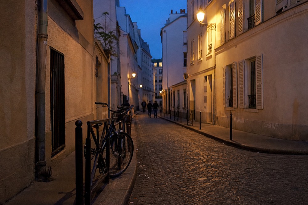A quiet cobbled street in central Verona at dusk with warm lamplight on stone facades, no text, no logos, no people