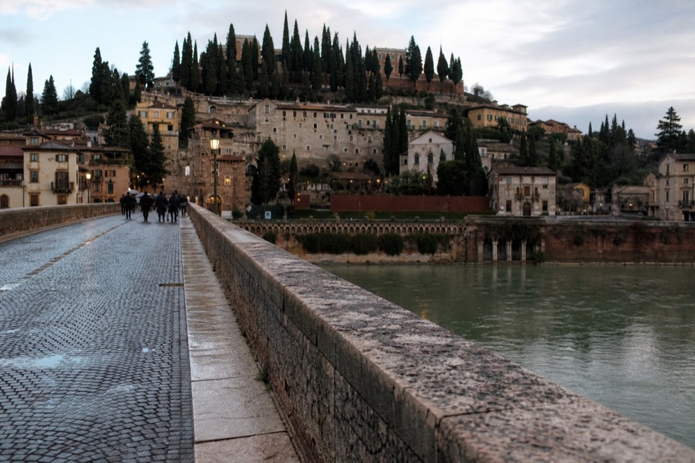 Ponte Pietra bridge over the Adige river with Veronetta hillside houses above, no text, no logos, no people