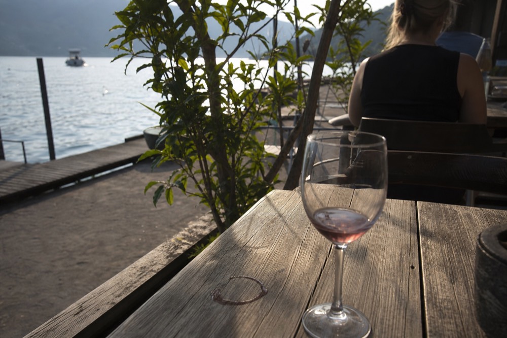 A glass of light red Bardolino wine on a wooden table beside the lake, no text, no logos, no people