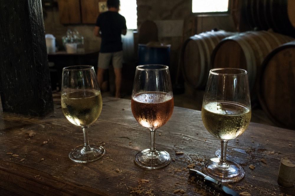 A tasting flight of three wines on a wooden counter in a Garda cellar, no text, no logos, no people