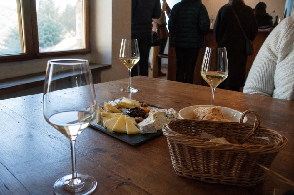 A tasting room with glasses of white wine and a platter of local cheese, no text, no logos, no people