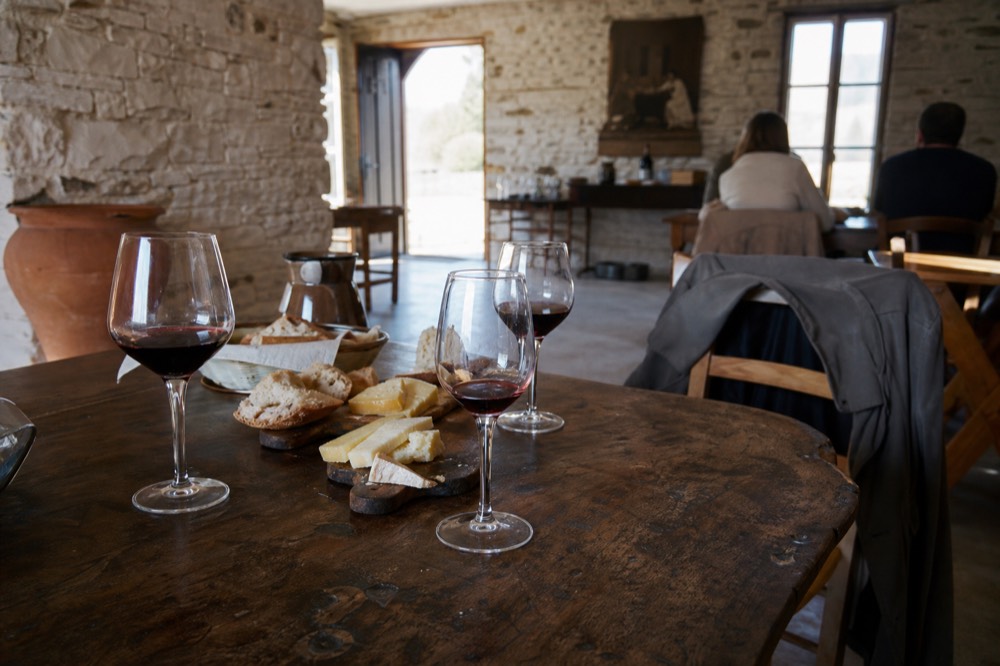 A rustic tasting room with glasses of red wine and a wooden table set with bread and cheese, no text, no logos, no people
