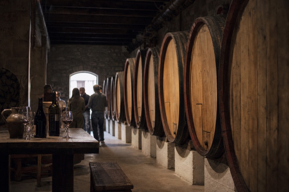 A row of large oak barrels in a dimly lit cellar, with a tasting table set up in the foreground, no text, no logos, no people