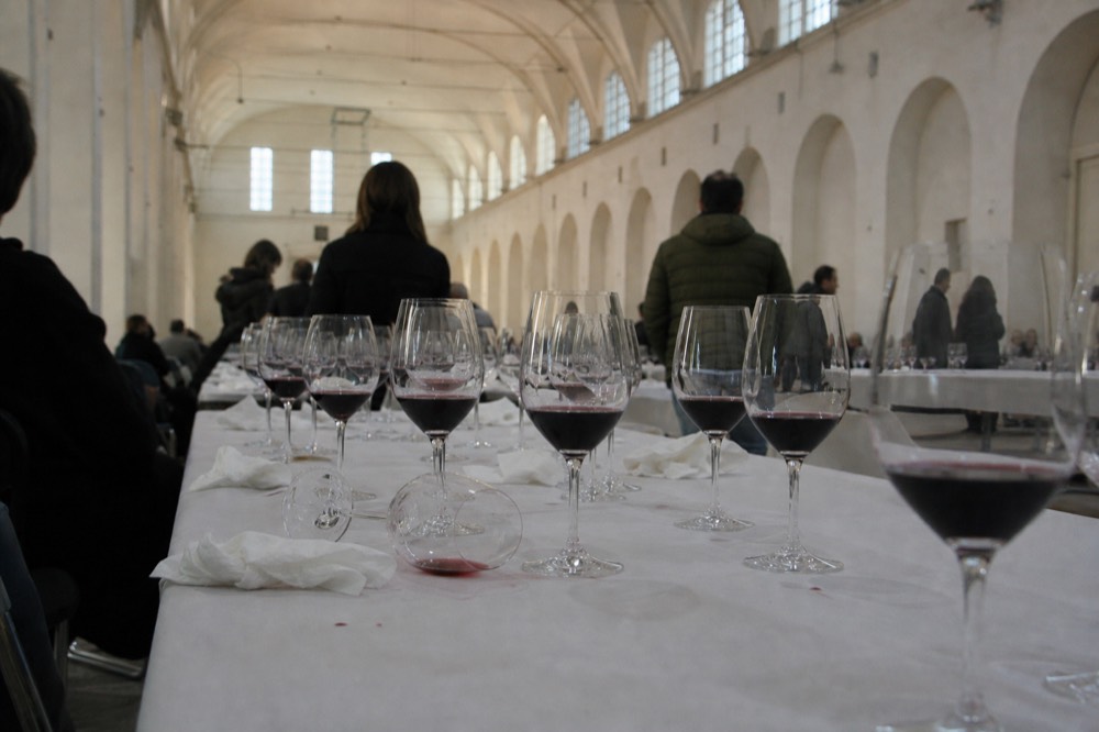 Glasses of red wine on a tasting table in a large hall, no text, no logos, no people