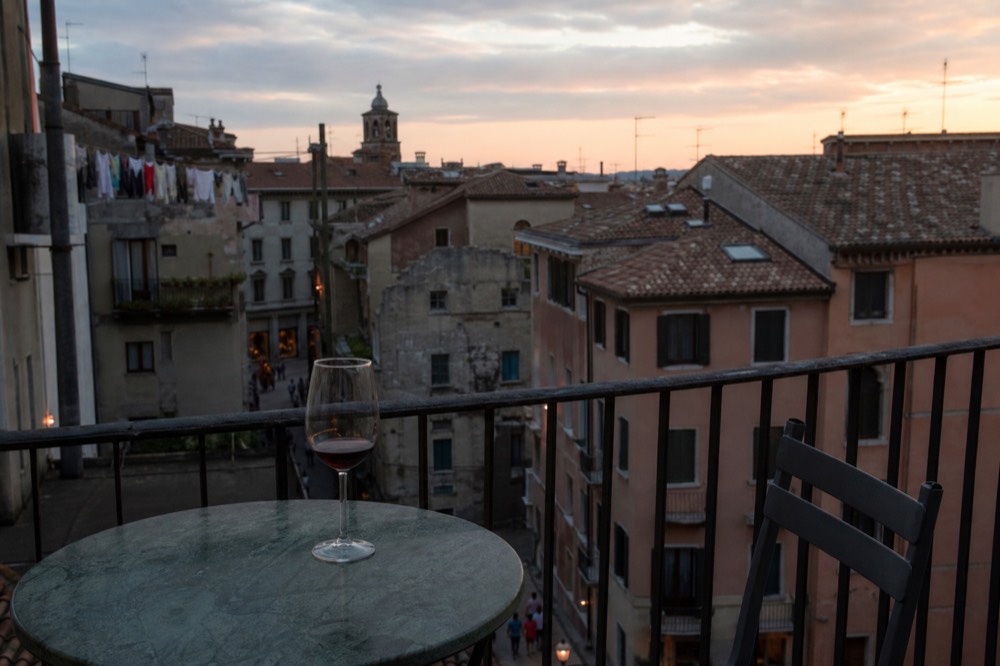 Evening light over rooftops and a wine glass on a table in Verona, no text, no logos, no people