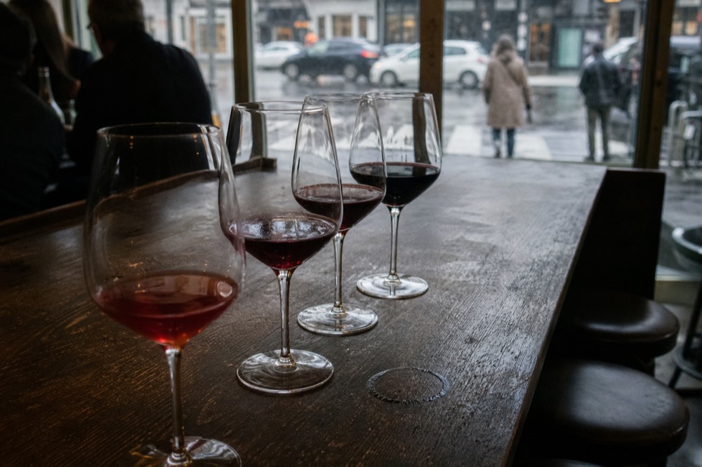 A tasting flight of red wines lined on a wooden bar counter, no text, no logos, no people