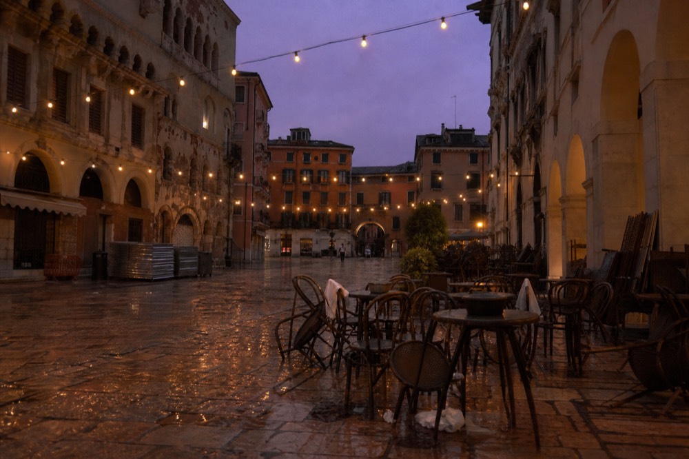 Crowd-free evening piazza in Verona with cafe tables and string lights, no text, no logos, no people