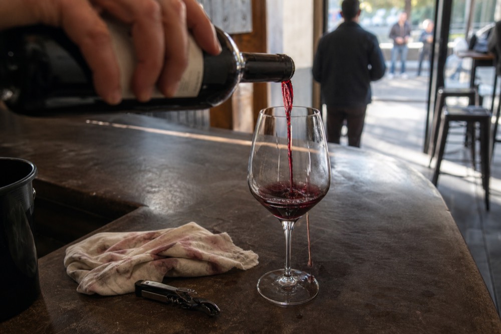 Sommelier hands pouring red wine into a glass on a counter, no text, no logos, no people